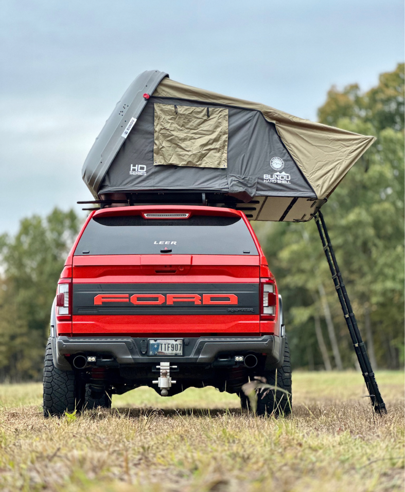 Red Ford truck with rooftop tent set up in a grassy area.