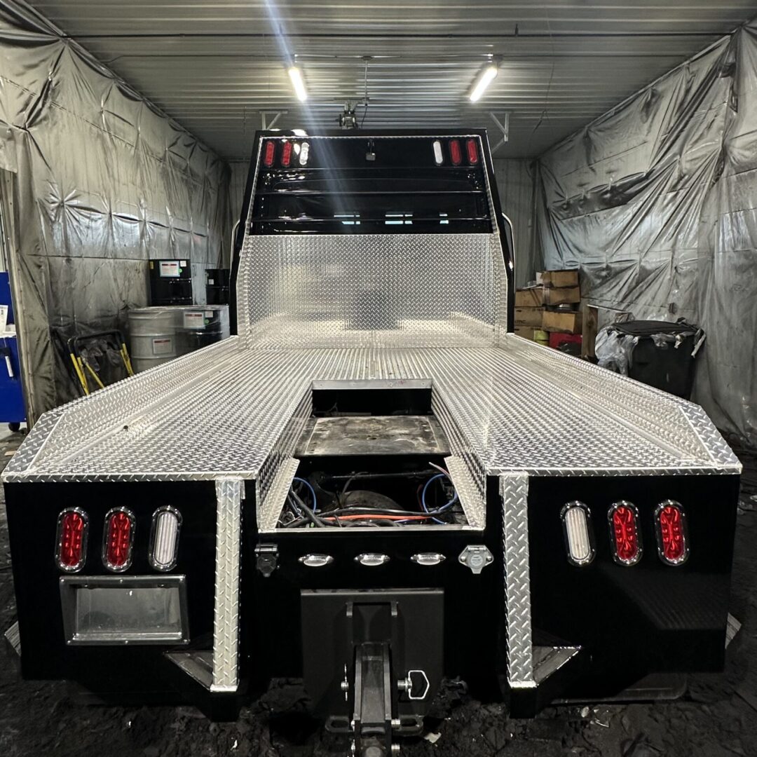 Rear view of a flatbed truck in a workshop with tail lights and hitch.