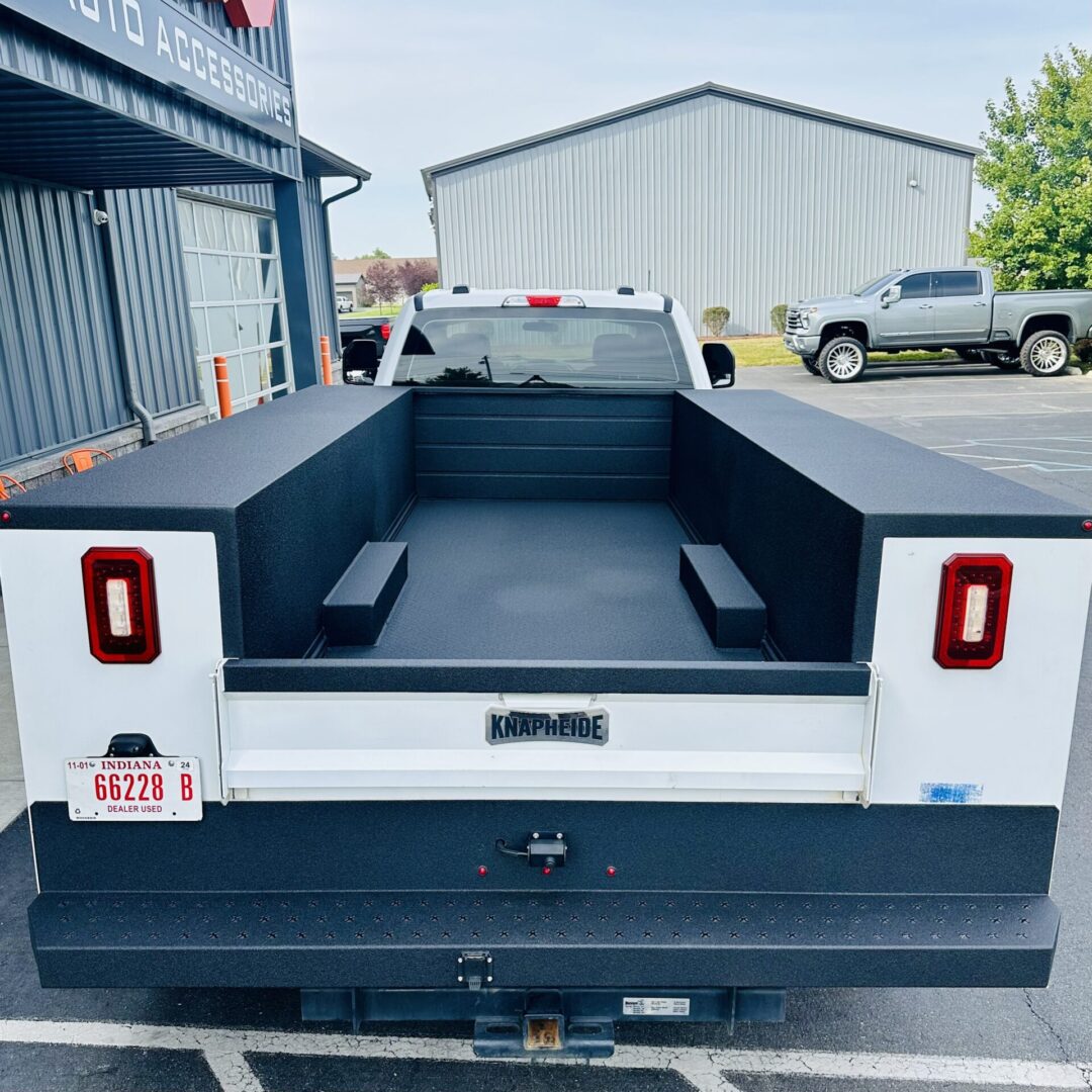 Empty white pickup truck bed with black liner in an industrial area.