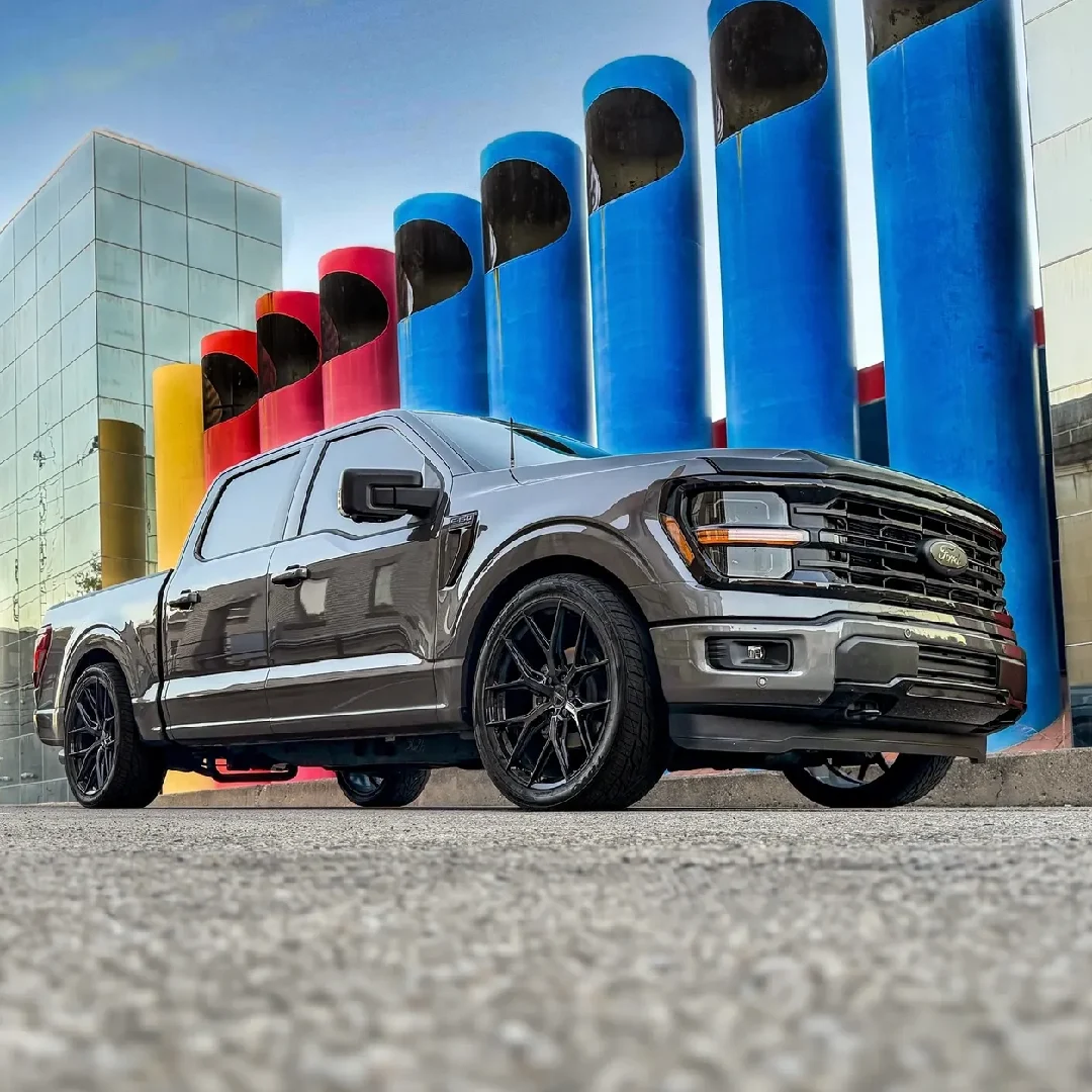 Black pickup truck parked near colorful industrial pipes.