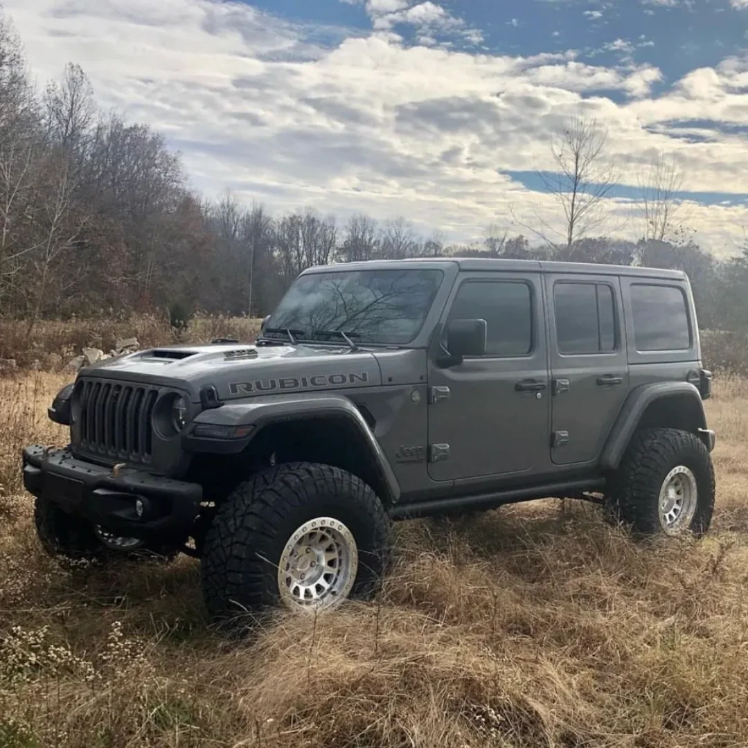 A rugged black Jeep Wrangler parked in a grassy field under a cloudy sky.