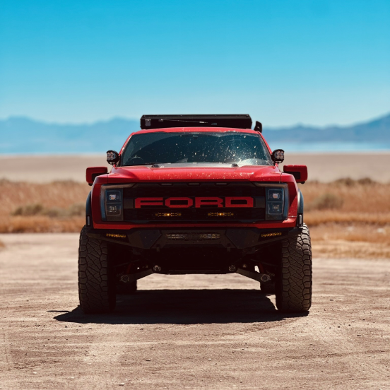 Red Ford truck parked on a desert road with mountains in the background.